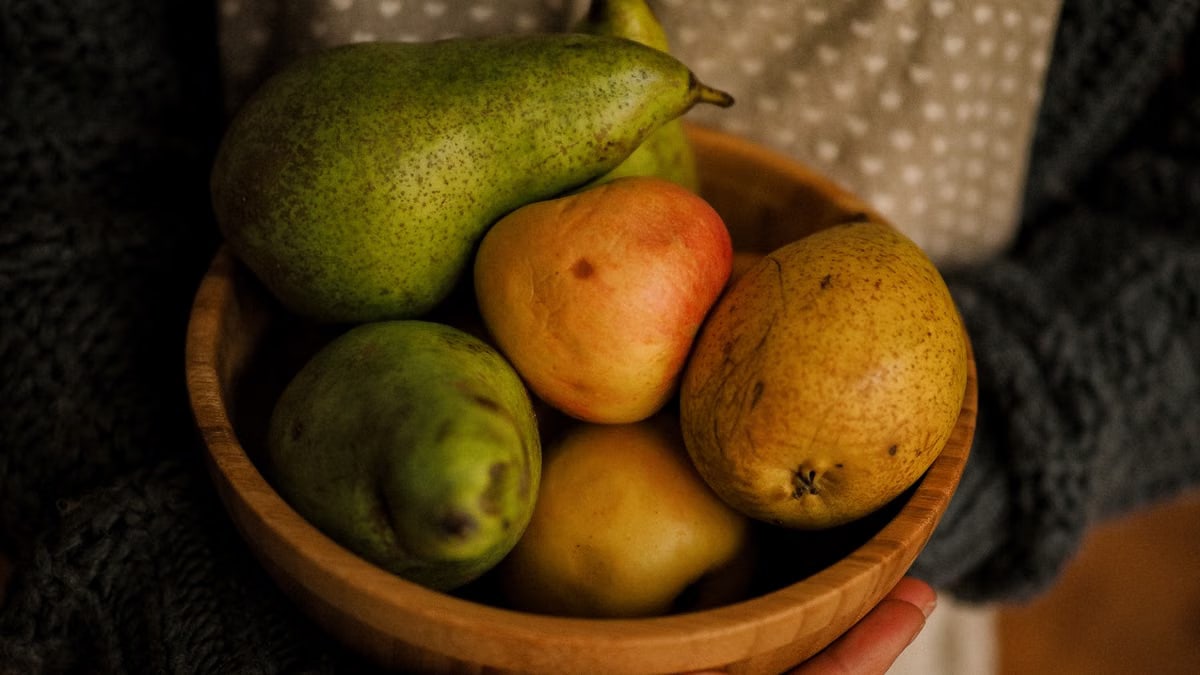 A wooden bowl filled with fresh pears, held outdoors on a sunny day.